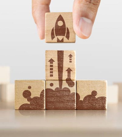 Business start up, start, new project or new idea concept. Wooden blocks with launching rocket graphic arranged in pyramid shape and a man is holding the top one.